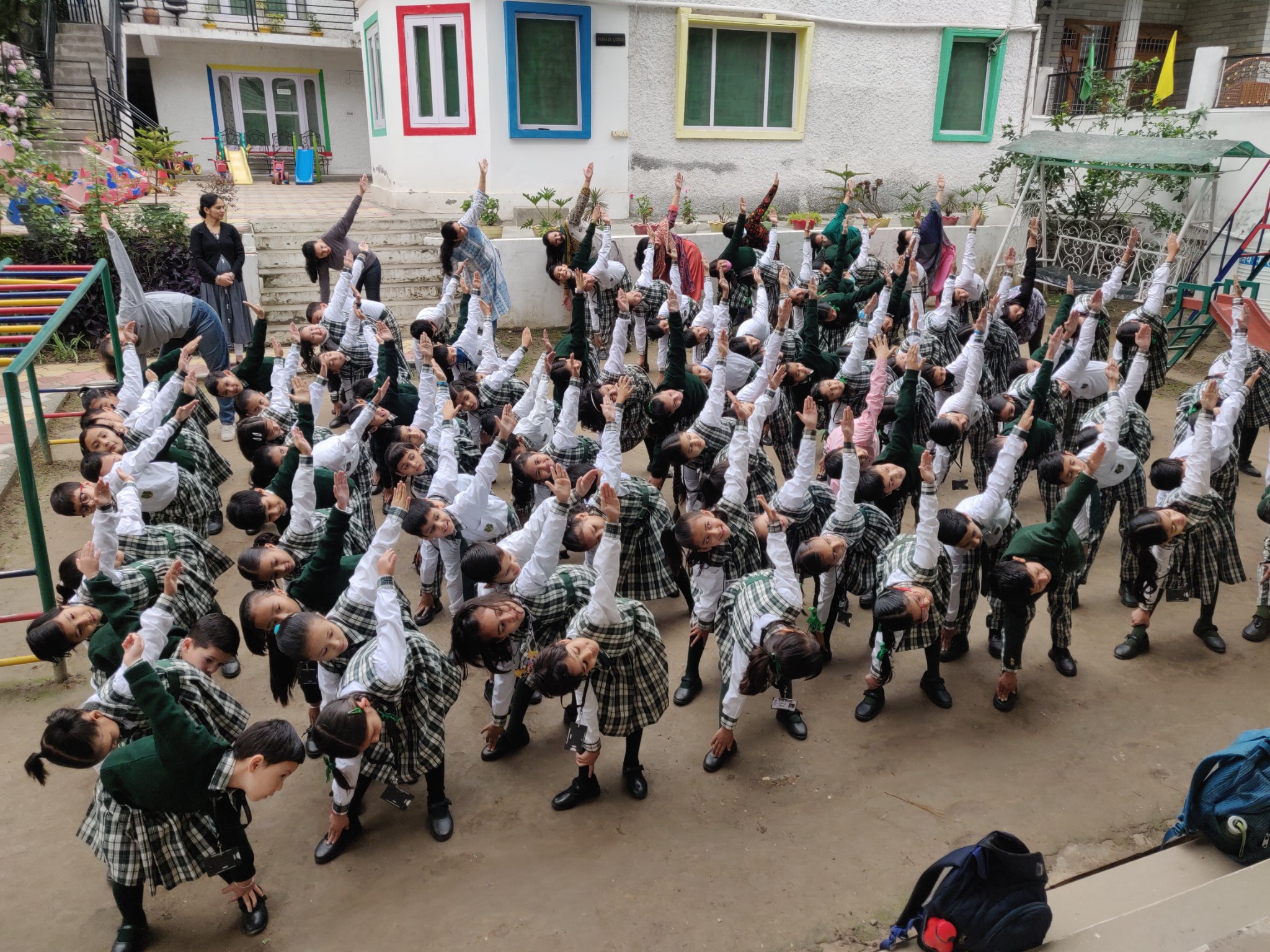 Students in green uniforms doing coordinated yoga stretches outdoors